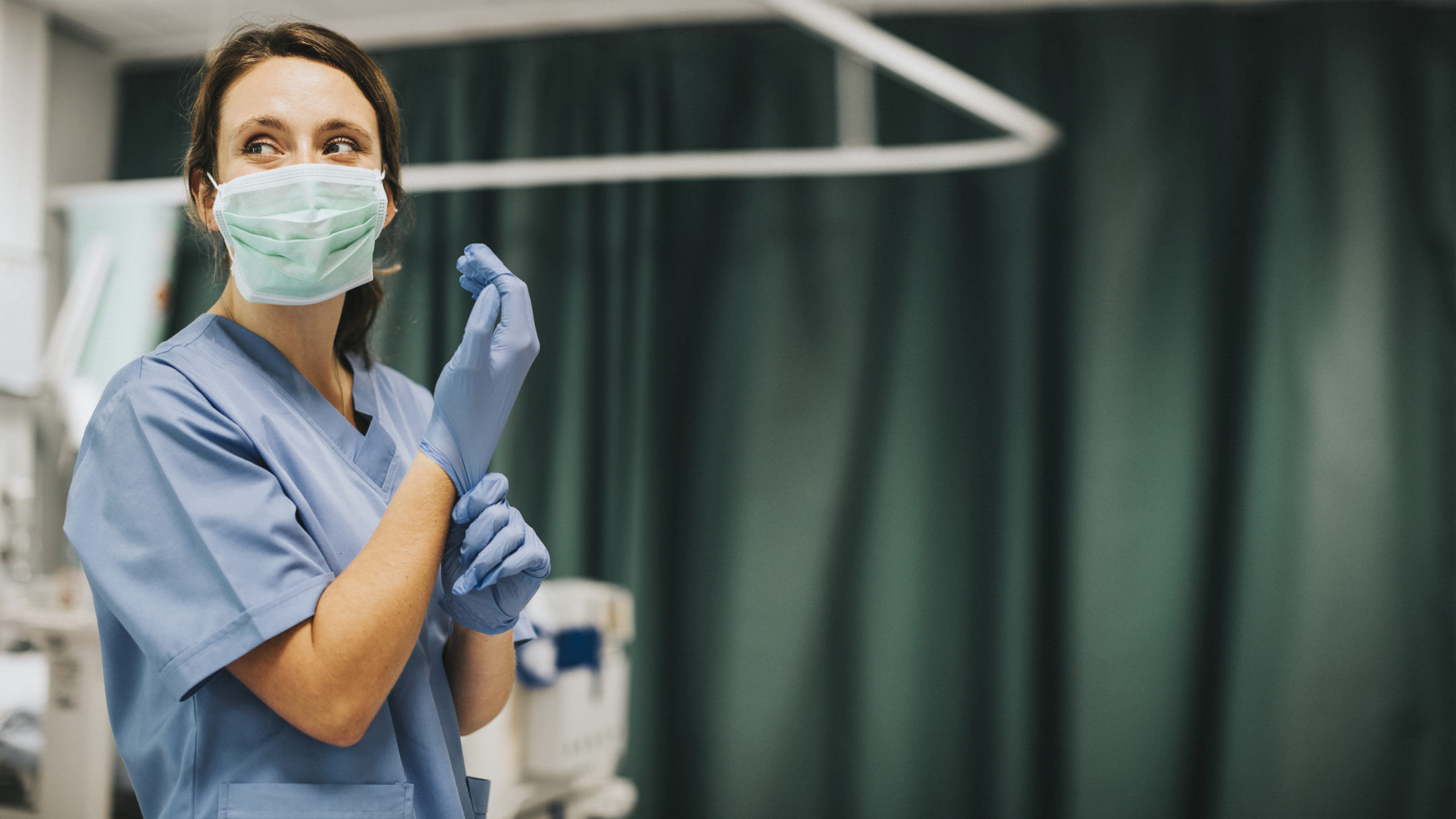 Female nurse with a mask putting on gloves preparing to cure coronavirus patient